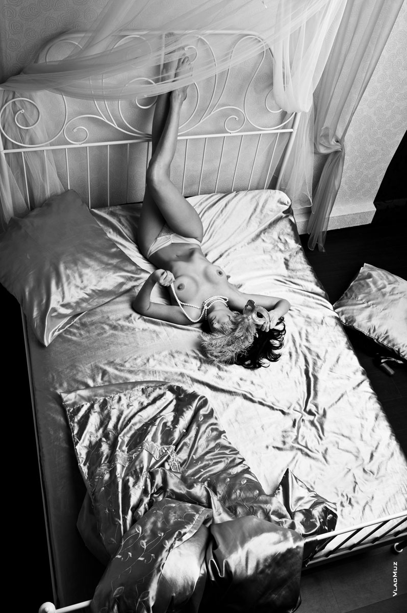 Фото сверху обнаженной девушки в маске, лежащей на кровати