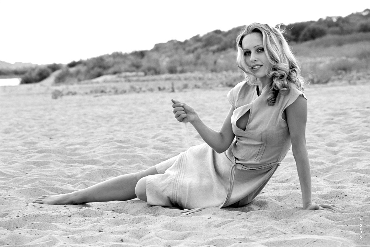 Черно-белая фотография девушки на песчаном пляже в платье, сидя на песке