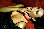 Модный фотопортрет девушки в черном платье, с рукой у губ, лежа на красном диване