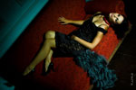 Фотография девушки-модели в черном коротком платье в полный рост, лежащей на красном диване