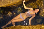 Фото модели сверху в полный рост в купальнике, девушка лежит в воде между камней