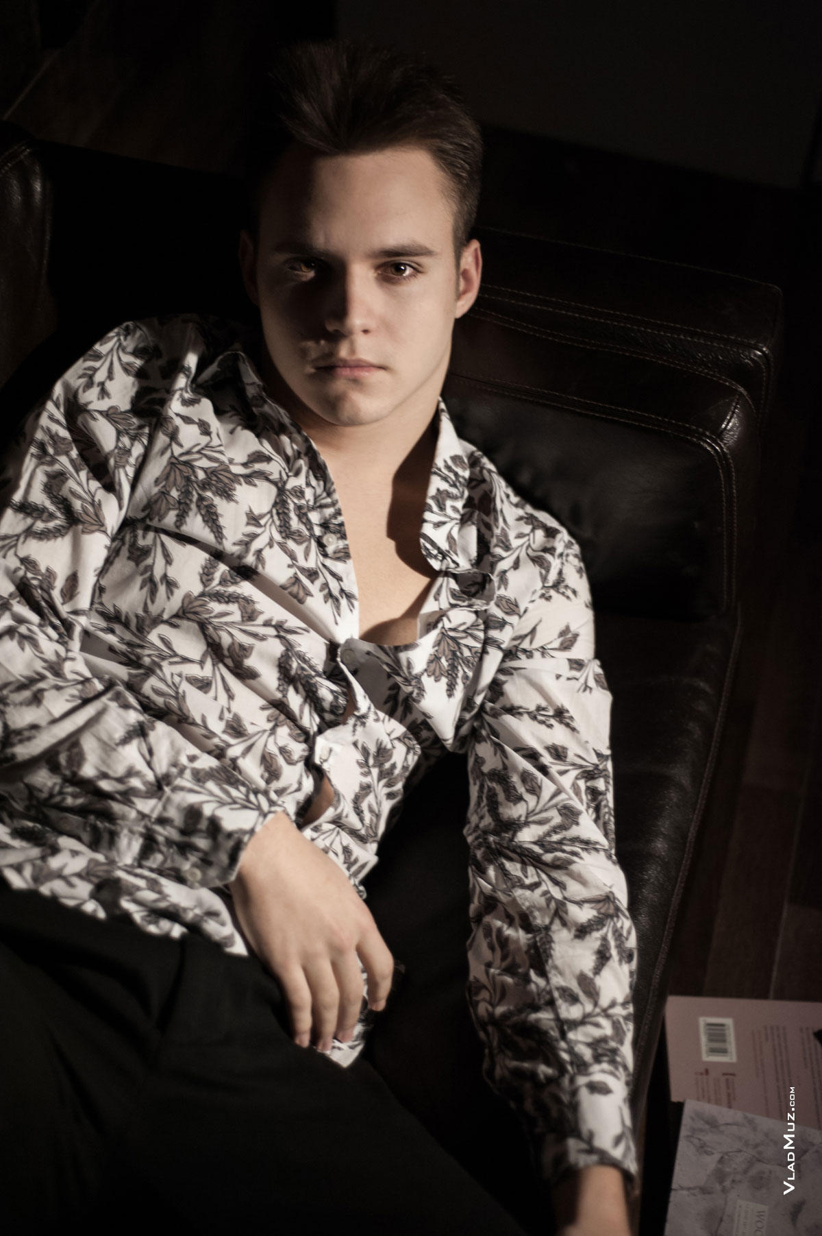 Фотопортрет юноши в темной тональности, лежа на диване, из мужского модельного портфолио